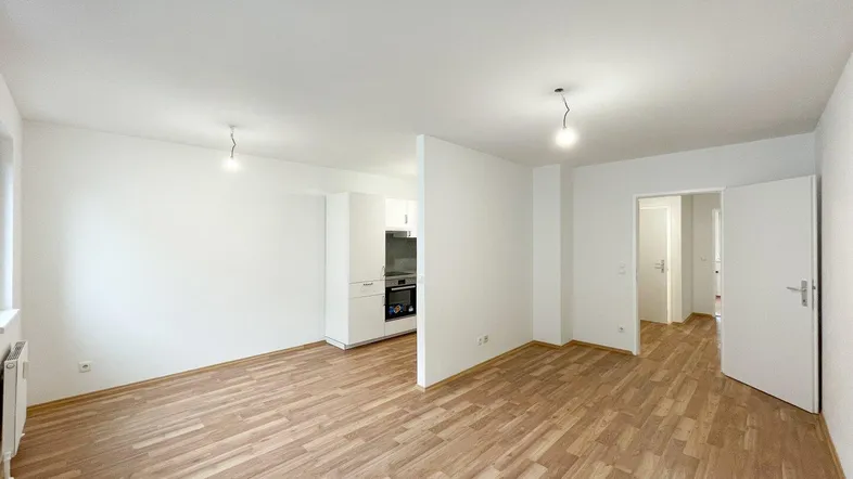 Heller Wohnbereich mit Laminatboden und teilweiser Sicht auf die integrierte Küchenzeile.