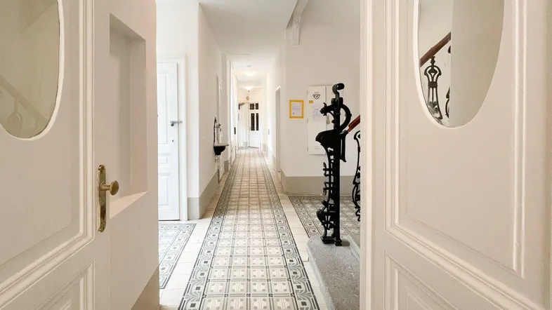 Langer Flur mit gemusterten Fliesenboden und Zugang zu verschiedenen Räumen in einem Altbau.