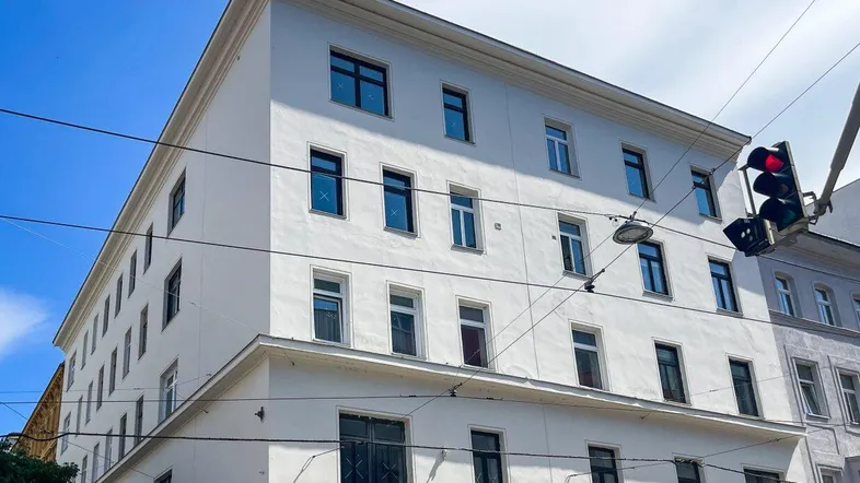 Weißes Mehrfamilienhaus mit mehreren Stockwerken und Geschäftsräumen im Erdgeschoss unter blauem Himmel.
