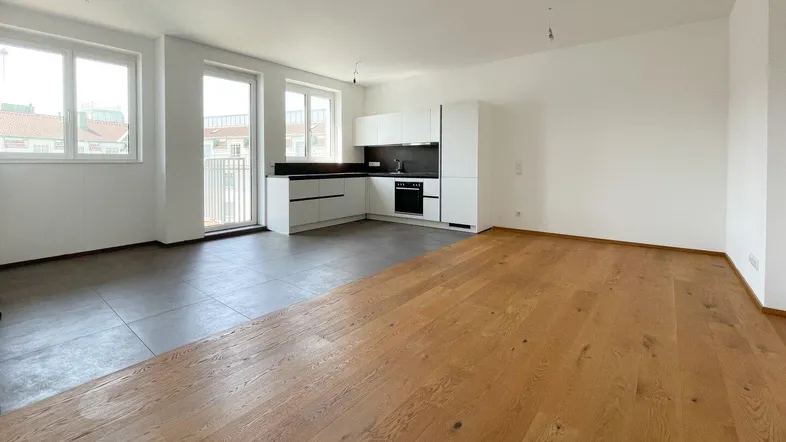 Heller, offener Wohnbereich mit integrierter Küche, Parkettboden und Zugang zum Balkon.