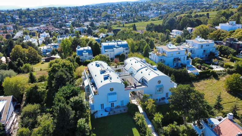 Luftaufnahme einer modernen Wohnanlage mit markanten Dächern, umgeben von viel Grün und einer weiten Landschaft.