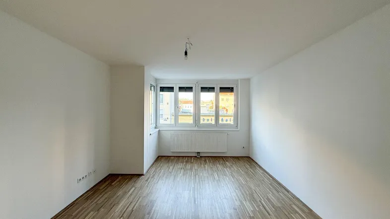 Geräumiger, heller Wohnbereich mit Parkettboden und Blick nach draußen durch die Fenster.