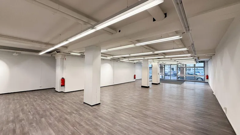 Großer, leerer Gewerberaum mit modernem Laminatboden und heller Deckenbeleuchtung.