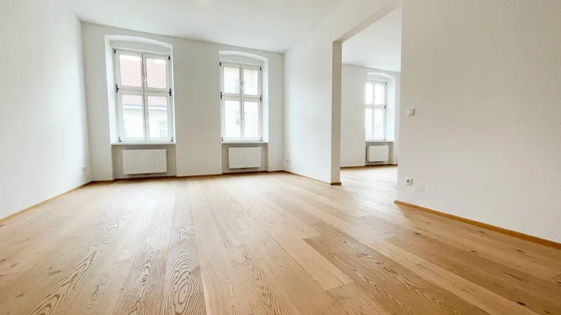 Helles, leeres Zimmer mit neuem Parkettboden und zwei Fenstern, bereit zur individuellen Gestaltung.