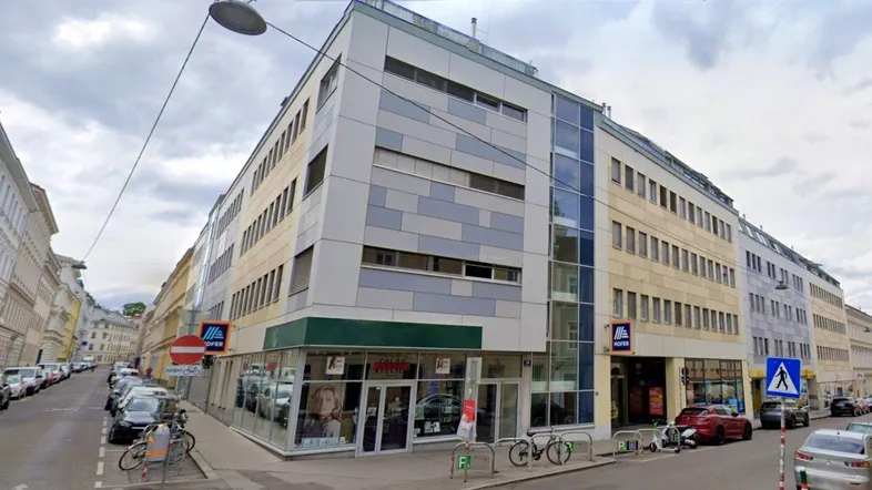 Modernes Eckgebäude an einer belebten Straße mit Geschäften im Erdgeschoss und Wohnungen darüber.