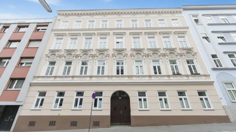 Historische Fassade eines Mehrfamilienhauses mit vielen Fenstern und dekorativen Elementen an der Straße.
