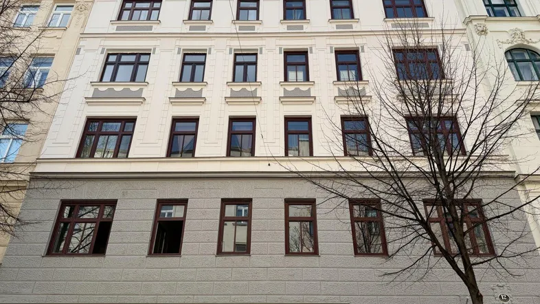 Die Vorderansicht des Gebäudes zeigt eine klassische Fassade mit vielen Fenstern und einem Geschäft im Erdgeschoss.