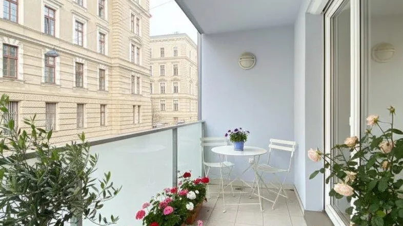 Heller Balkon mit Fliesenboden, Sitzgelegenheiten und Blick auf die Stadtgebäude.