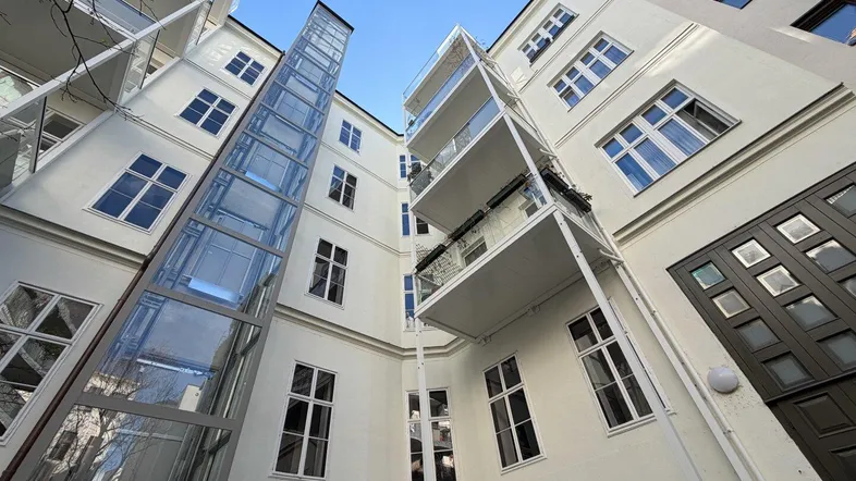 Blick auf den Innenhof eines modernen Gebäudes mit Glasaufzug und Balkonen.