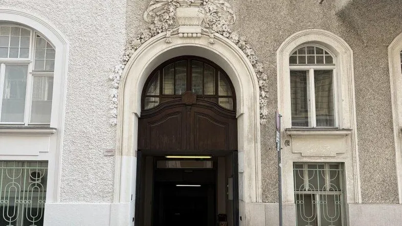 Historische Fassade eines Gebäudes mit einem kunstvoll verzierten Torbogen und klassischen Fenstern, die den Eingang schmücken.