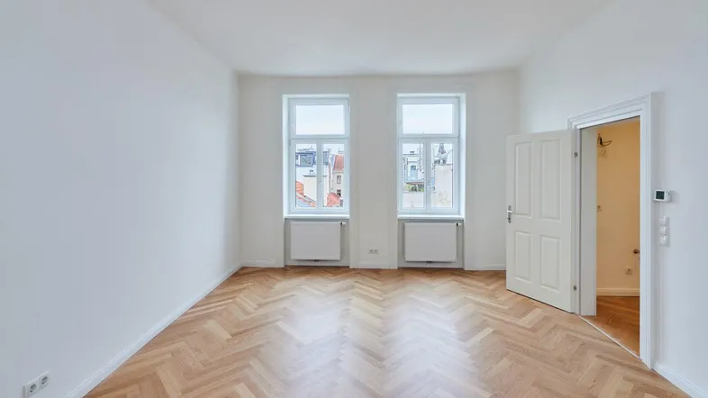 Helles, leeres Zimmer mit Fischgrätparkettboden und zwei Fenstern, bereit zur Einrichtung.