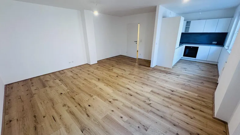 Heller offener Wohnbereich mit neuem Holzboden und integrierter Küchenzeile, ideal für modernes Wohnen.
