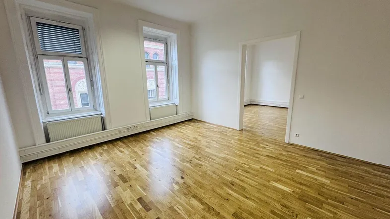 Heller Büroraum mit Holzboden und zwei großen Fenstern, die viel Tageslicht hereinlassen.