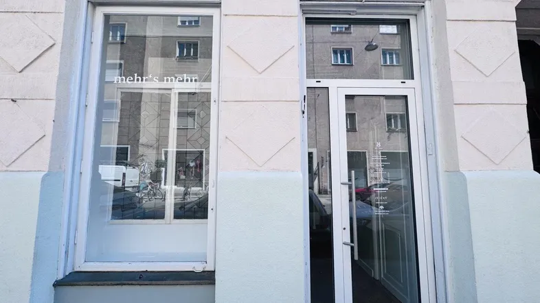 Eingangsbereich eines Geschäfts mit großen Schaufenstern und einer modernen Glastür, die viel Tageslicht hereinlässt.