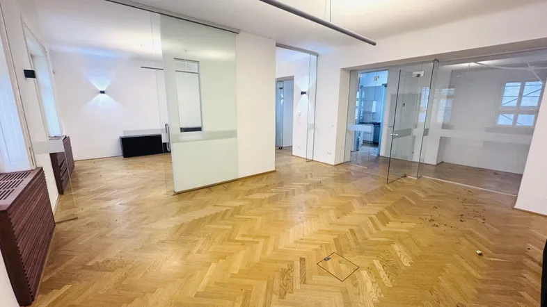 Geräumiger Bürobereich mit Fischgrätparkett, modernen Glasabtrennungen und viel Tageslicht.