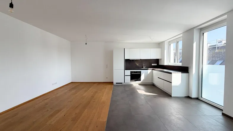 Heller offener Wohnbereich mit moderner Einbauküche, Holzboden und Zugang zu einem Balkon oder Terrasse.