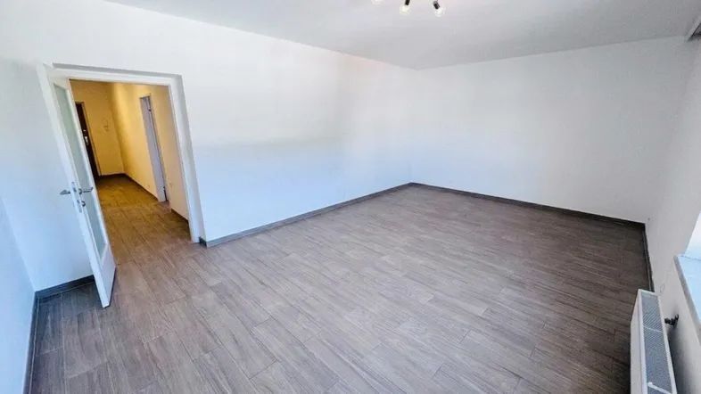 Helles, leeres Zimmer mit modernem Laminatboden und weiß gestrichenen Wänden, bereit zur Einrichtung.