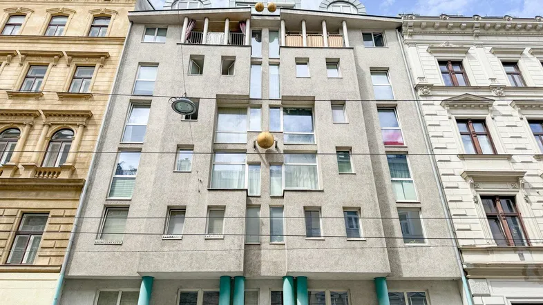 Modernes Gebäude mit markanter Fassade, Balkonen und dekorativen Säulen in urbaner Umgebung.