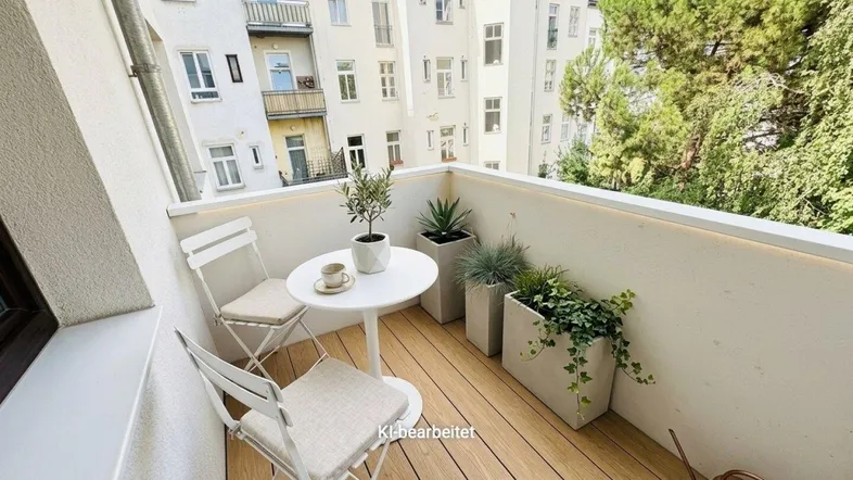 Gemütlicher Balkon mit Holzdielenboden, Pflanzen und Sitzgelegenheiten, bietet einen Blick auf die umliegenden Gebäude.