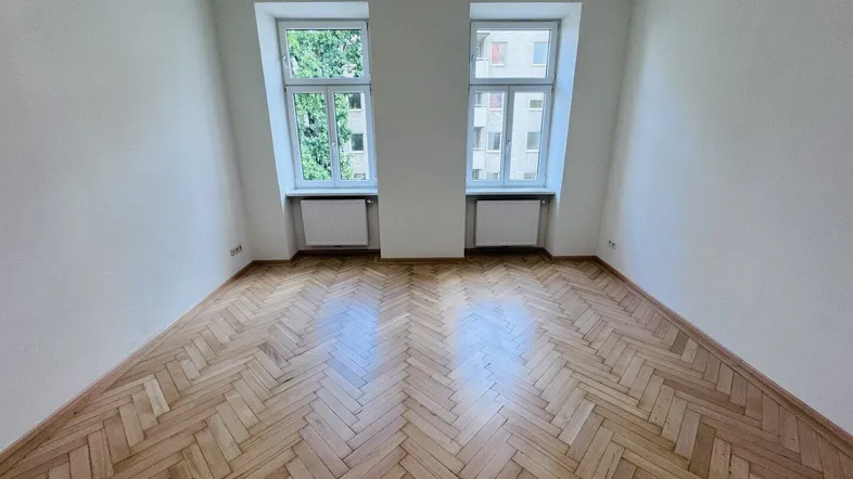Heller Raum mit Fischgrätparkettboden und zwei Fenstern, ideal als Wohn- oder Schlafzimmer.
