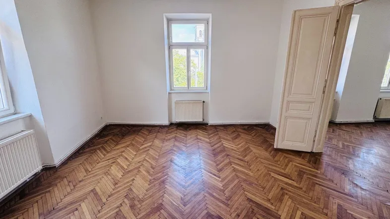 Heller Raum mit elegantem Fischgrätparkett und einer klassischen Holztür, die zu einem weiteren Zimmer führt.