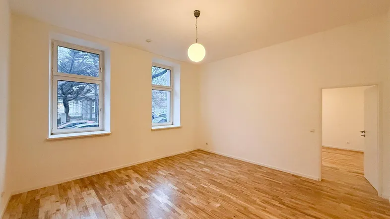 Helles Wohnzimmer mit Holzboden und zwei großen Fenstern, die viel Tageslicht hereinlassen.