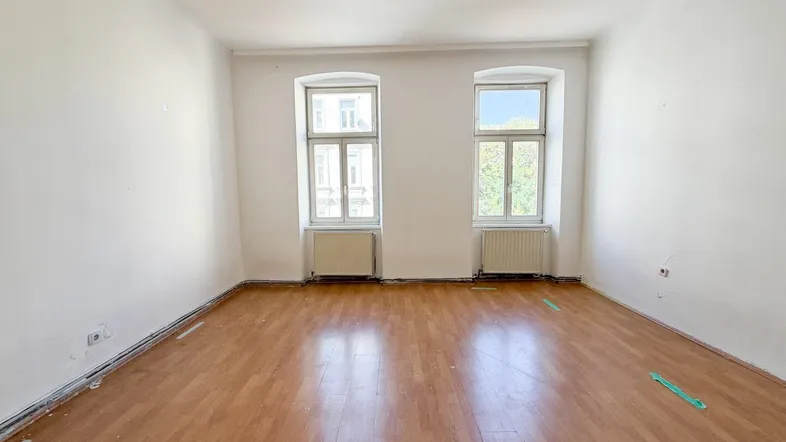 Helles Zimmer mit Holzboden und zwei Fenstern, bereit zur individuellen Gestaltung.