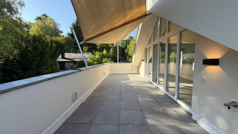 Geräumige Dachterrasse mit Fliesenboden, ausfahrbarer Markise und Blick ins Grüne.