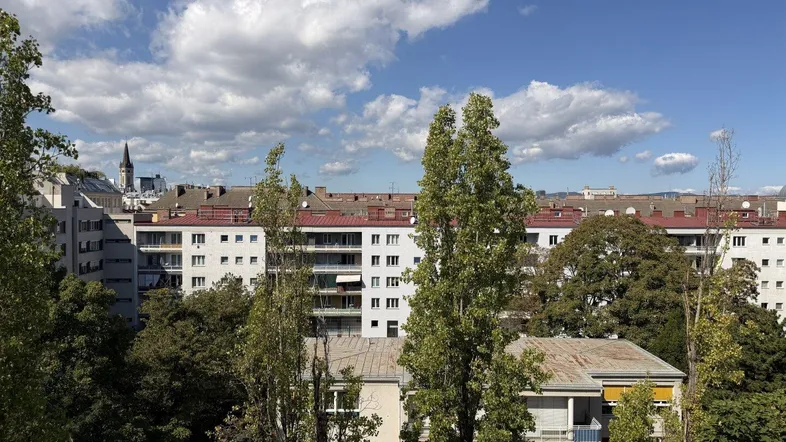Panoramablick über die Stadt mit Wohngebäuden, Bäumen und einem Kirchturm am Horizont.