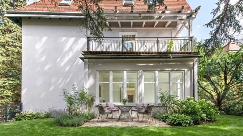 Charmantes Haus mit gepflegtem Garten, sonniger Terrasse und Balkon im Obergeschoss, umgeben von viel Grün.