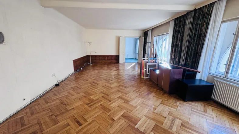 Geräumiges Wohnzimmer mit Fischgrätparkett, hohen Fenstern und viel Tageslicht.