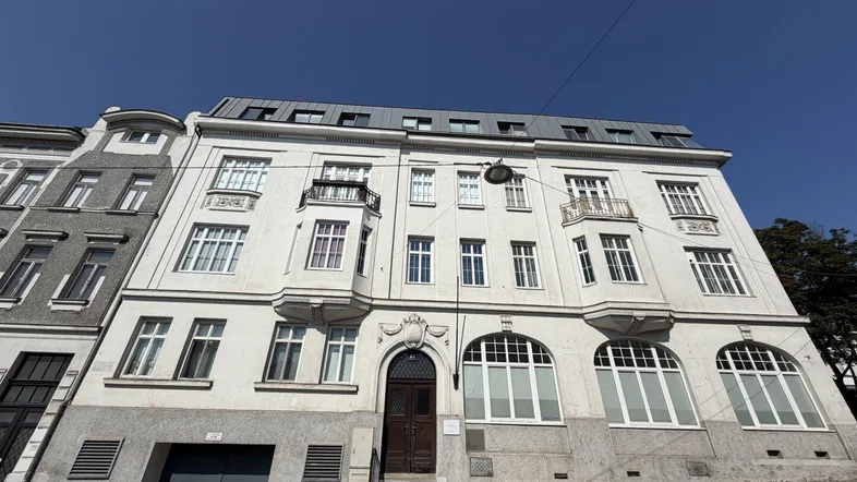 Historische Fassade eines Mehrfamilienhauses mit großen Fenstern und Mansarddach.