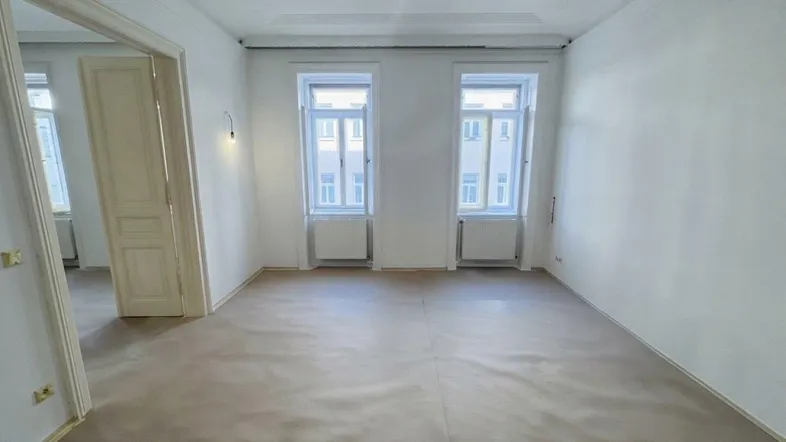 Helles, leeres Zimmer mit zwei Fenstern und hellem Boden, bereit zur individuellen Gestaltung.