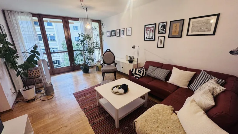 Helles Wohnzimmer mit Holzboden, rotem Sofa und Zugang zu einem Balkon oder einer Terrasse.