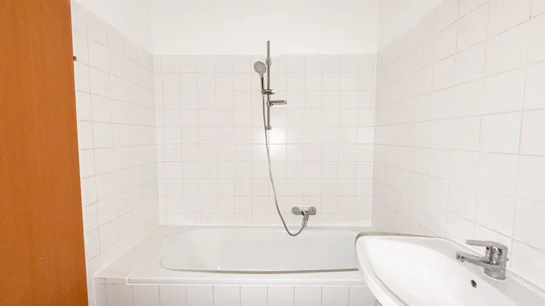 Weiß gefliestes Badezimmer mit Badewanne und Waschbecken, in einem einfachen, funktionalen Zustand.