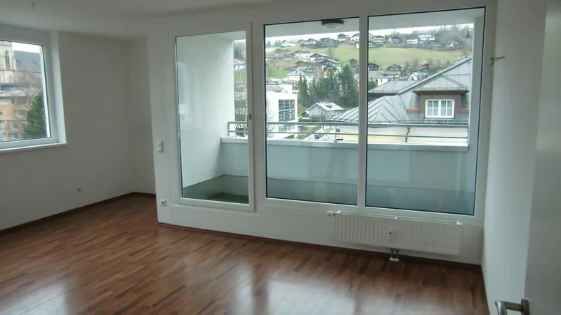 Helles Zimmer mit Holzboden, großen Fenstern und Zugang zu einem Balkon mit Bergblick.
