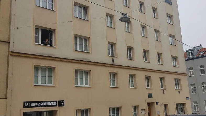 Mehrstöckiges Wohngebäude mit hellbeiger Fassade und vielen Fenstern an einer Stadtstraße.