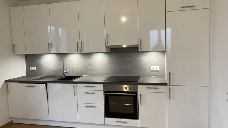 Moderne Einbauküche mit weißen Hochglanzfronten, integrierten Geräten und dunkler Arbeitsplatte.
