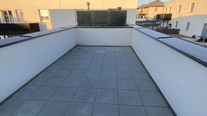 Geräumige Dachterrasse mit Fliesenboden und Blick auf die umliegenden Neubauten.