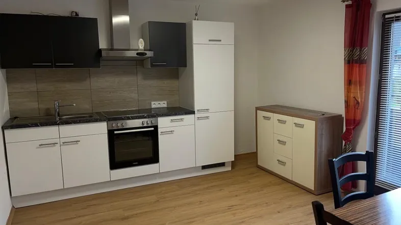 Moderne Küche mit weißen und schwarzen Schränken, integriertem Backofen und Holzboden, daneben ein Essbereich.