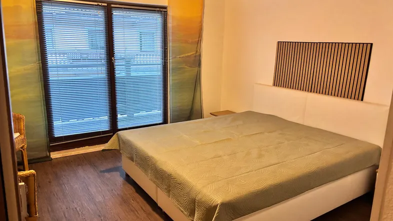 Helles Schlafzimmer mit großem Doppelbett, Holzboden und Zugang zum Balkon.