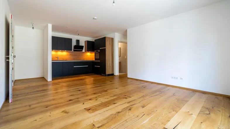 Heller offener Wohnbereich mit moderner Einbauküche und hochwertigem Holzfußboden.