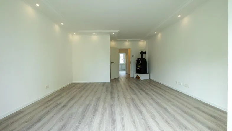 Helles Wohnzimmer mit modernem Kaminofen, hellem Laminatboden und indirekter Deckenbeleuchtung.