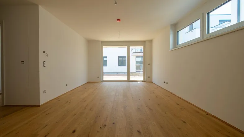 Helles, leeres Wohnzimmer mit neuem Parkettboden und Zugang zu einem Außenbereich.