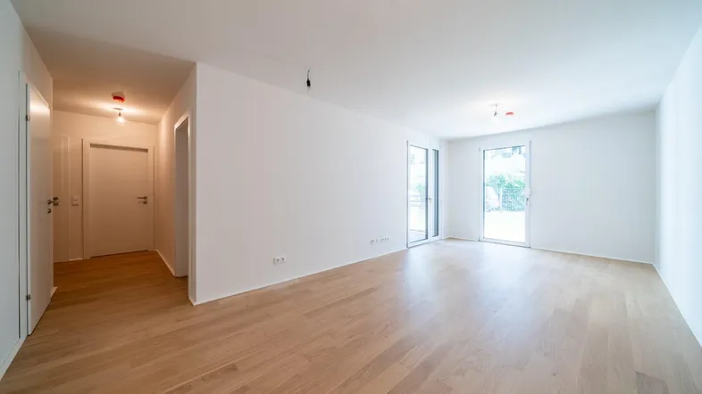 Helles, leeres Zimmer mit Parkettboden und Zugang zu einem Außenbereich.
