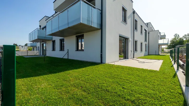Moderne Wohnanlage mit gepflegtem Rasen, Terrasse und Balkonen, umgeben von Neubauten.