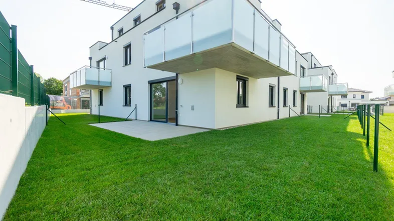 Modernes Gebäude mit gepflegtem Rasen, kleiner Terrasse und Balkonen im Neubaugebiet.