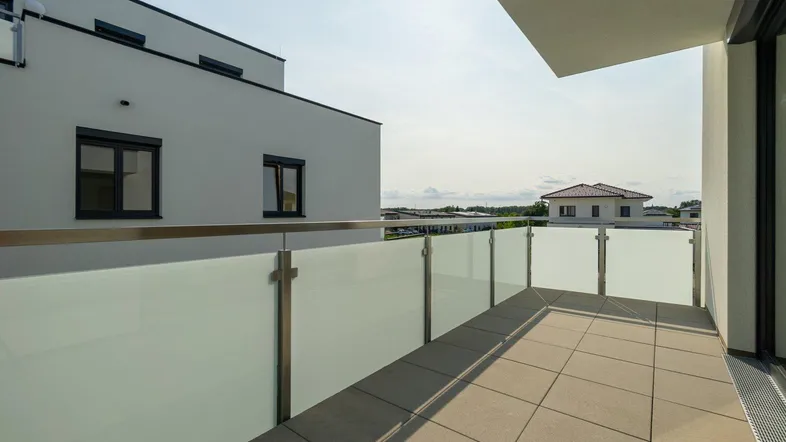 Heller Balkon mit Glasbrüstung und Blick auf die umliegenden Gebäude und Landschaft.