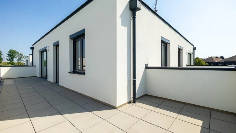 Große, geflieste Terrasse an einem modernen Gebäude unter blauem Himmel.
