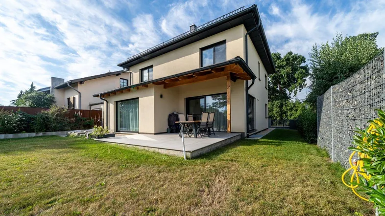 Rückseite des modernen Hauses mit großer Rasenfläche und überdachter Terrasse.